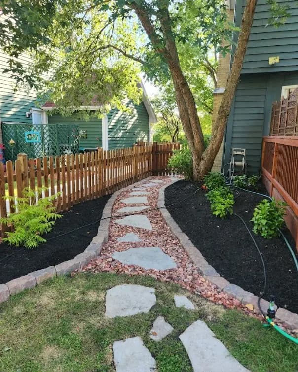 Completed curved stone walkway with fresh planting beds.
