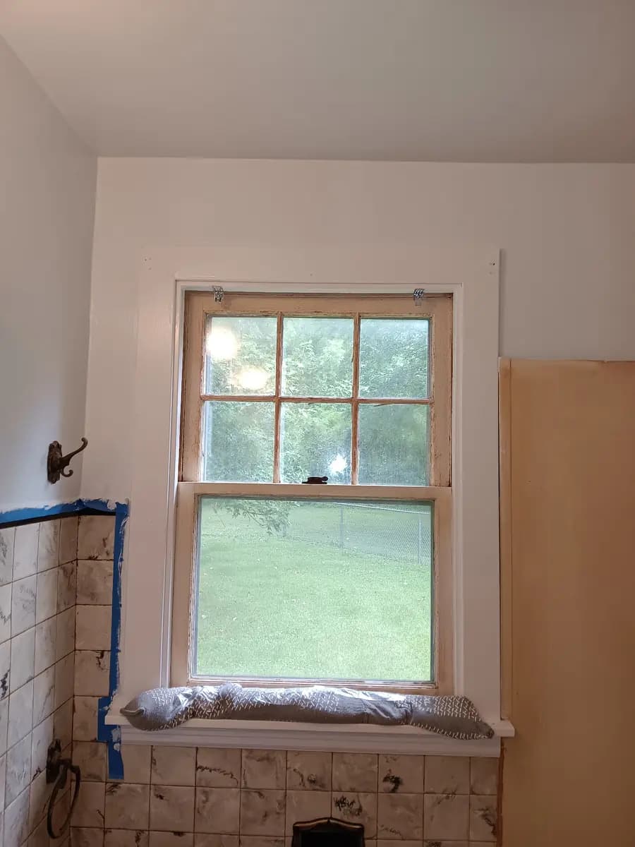 Repainted window trim above the tub; original tile still masked for protection.