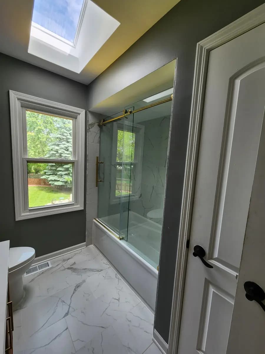Finished bathroom view showing the glass enclosure, window, and tiled floor.