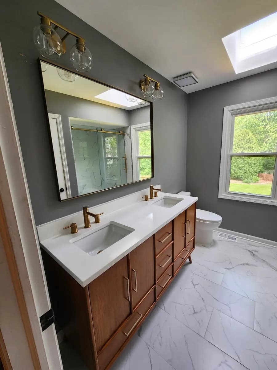 Completed bathroom renovation with double vanity, brass fixtures, and a window.